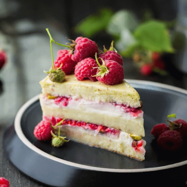 Raspberry layer cake slice with frest
                    raspberries ont top. Served on a fance plate.